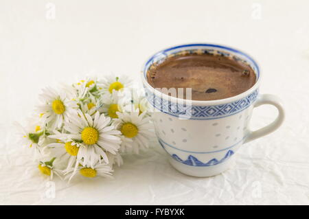 Kamille Bouquet und Coffe Cup auf weißen Textilien Stockfoto