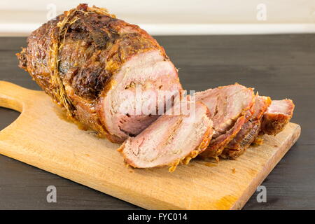 Gerollte Schweinefleisch auf ein Schneidebrett auf einem schwarzen Tisch geröstet Stockfoto