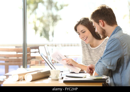 Gruppe von zwei Kollegen arbeiten vergleichende Prognose Grafiken in einem Café mit einem Fenster im Hintergrund Stockfoto