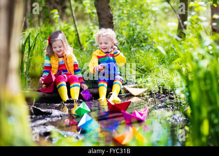 Kinder spielen mit bunten Papierschiffchen in einem kleinen Fluss an einem sonnigen Frühlingstag. Kinder spielen, die Natur zu erforschen. Stockfoto