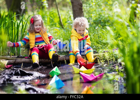 Kinder spielen mit bunten Papierschiffchen in einem kleinen Fluss an einem sonnigen Frühlingstag. Kinder spielen, die Natur zu erforschen. Stockfoto