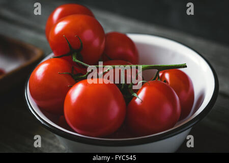 Frische Tomaten an Rebstöcken in Schüssel auf rustikalen Holztisch. Tiefenschärfe, getönten Bild Stockfoto