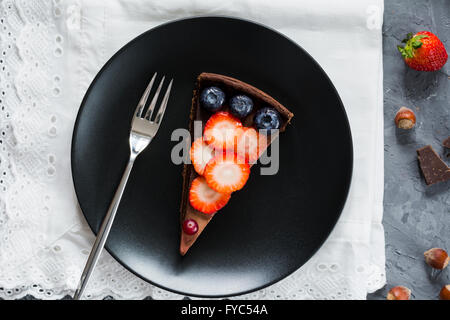 Scheibe von Mousse au Chocolat Torte (Kuchen) garniert mit Erdbeeren, Blaubeeren und Preiselbeeren auf schwarzen Druckplatte. Tabelle-Draufsicht Stockfoto