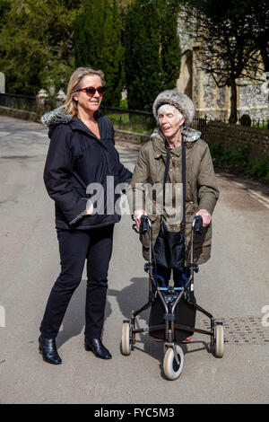 Einen weiblichen Verwandten zu Fuß mit einer behinderten älteren Frau mit einer drei-Rad Rollator, Sussex, UK Stockfoto