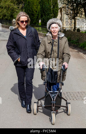 Einen weiblichen Verwandten zu Fuß mit einer behinderten älteren Frau mit einer drei-Rad Rollator, Sussex, UK Stockfoto