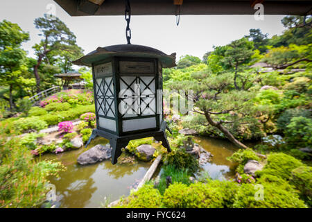 Eine traditionelle Metall Laterne hängen von einer Veranda mit Blick auf einen schönen japanischen Garten Stockfoto