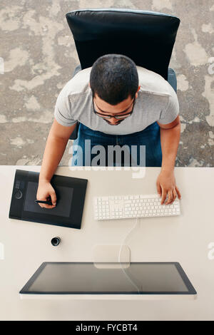 Männliche Grafik-Designer mit Grafiktablett für Entwurf und Zeichnung. Draufsicht der junge Mann, der an seinem Schreibtisch arbeitet. Stockfoto