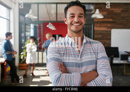 Porträt eines schönen jungen Geschäftsmannes Stand mit verschränkten in einem Büro. Intelligente kaukasischen jungen männlichen Designer mit seinem