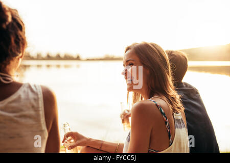 Porträt von lächelnden jungen Mädchen sitzen an einem See mit ihren Freunden. Junge Menschen, die einen Tag am See zu genießen. Stockfoto