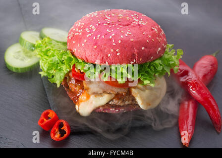 große rote Hamburger mit Rauch auf Schiefer Tisch. Stockfoto