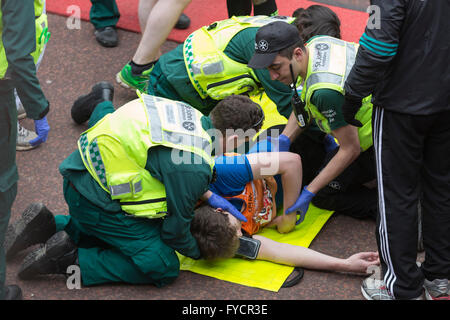 London, UK. 24. April 2016. Mediziner aus St John Ambulance helfen einen Läufer, der nach Überqueren der Ziellinie zusammengebrochen. Die 2016 beendet Geld Virgin London-Marathon auf der Mall, London, Vereinigtes Königreich. Stockfoto
