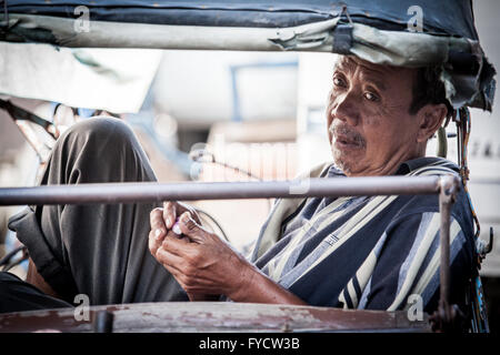 Fahrer von einem indonesischen Fahrradrikscha nimmt einen entspannenden Moment Verlegung im hinteren Teil der Kabine Stockfoto