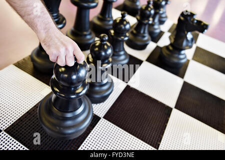 Hand bewegt den schwarzen Bauern auf einem Riesen-Schach-Spiel Stockfoto