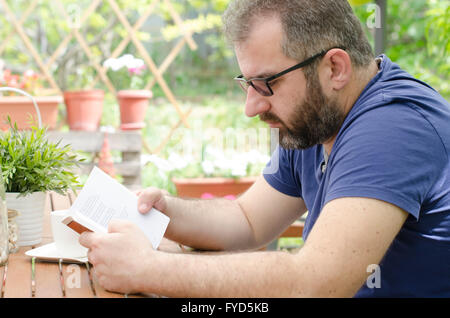 Mann auf einer Bank draußen sitzen und ein Buch lesen. Stockfoto