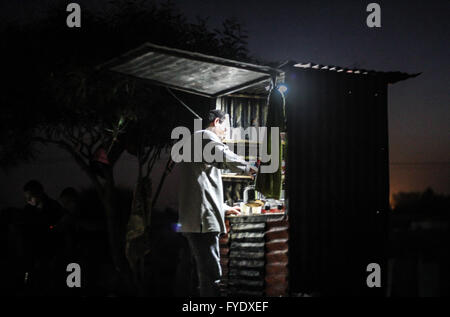 Gaza-Streifen, Khan Yunis, Mideast. 26. April 2016. Ein palästinensischer Mann Amin Fasfous arbeitet spät in die Nacht und Ladenbesitzer in einem kleinen Garten auf der einen Seite der Straße in den Westen von Khan Younis, die verkaufen heiße Getränke und einige Widgets, Menschen, Jugendliche und Kinder, die kommen, um mit ihm zu sitzen, die ihre Häuser wegen der häufigen Stromausfälle und warmen Klimazonen geflohen waren und ihre Anliegen und Leidensweg ausgeben. Ahmad Salem/Alamy Live-Nachrichten Stockfoto