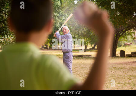 Großeltern mit Enkel: Senior Woman spielen Baseball mit seinem Enkel im Park. Der alte Mann hält die Fledermaus, whil Stockfoto