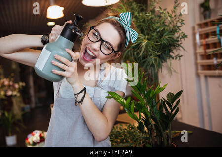 Amüsante junge Frau Floristen mit Wasser Sprayer, Blumen gießen und schreien Stockfoto