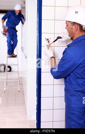 Elektriker eine Trittleiter eine Steckdose und ein Kollege anschrauben Stockfoto
