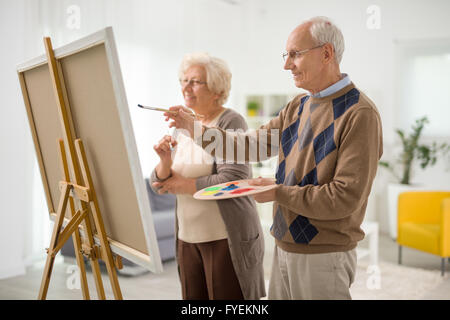 Älterer Mann und Frau malt etwas auf einer Leinwand mit Pinsel zu Hause Stockfoto