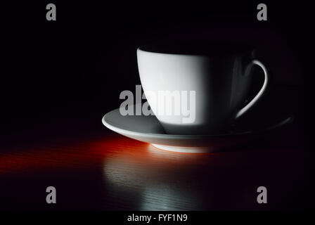 weiße Tasse auf Untertasse in Dunkelheit Stockfoto