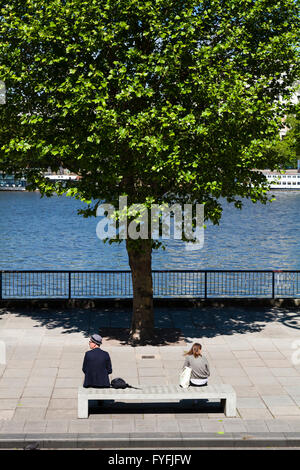 Zwei Menschen sitzen auf konkrete Bank von Fluß mit Baum, London, England, Vereinigtes Königreich Stockfoto