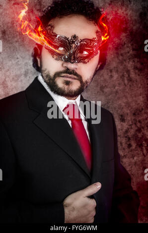 böser Mensch Konzept mit feurigen Augen und venezianische Maske trug schwarzes Kleid Stockfoto