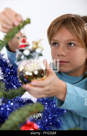 Kleiner Junge hängende Dekoration am Weihnachtsbaum Stockfoto