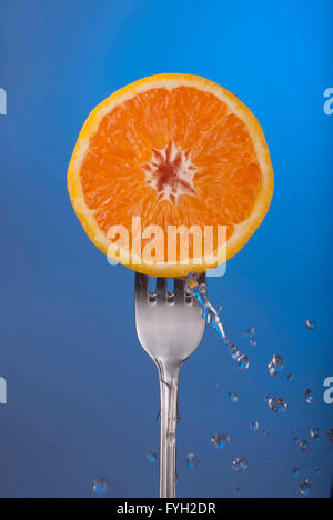 Köstliche orange Frucht halbieren auf Gabel mit Spritzwasser, blaue Farbe Hintergrundfoto Konzept. Stockfoto