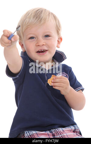 Kleinkind einen Keks essen und spielen mit Mamas Wimperntusche Zauberstab Stockfoto