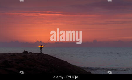 Silhouette der Fischer bei Sonnenuntergang, stehend ein Wellenbrecher Stein am Foradouro Strand, Portugal. Stockfoto