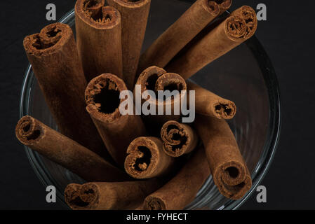 Top View Zimt Sticks stehen in Glasschale mit schwarzem Schiefer Schneidbrett im Hintergrund Stockfoto