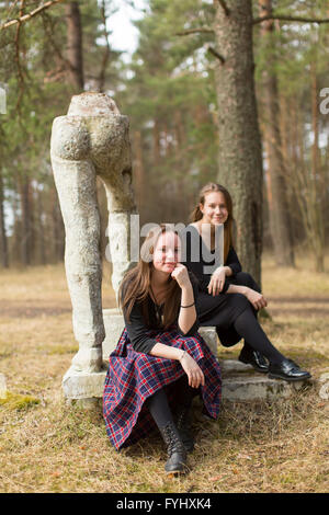 Zwei Freundinnen sitzen nahe dem zerstörten Soz-Art-Kunst-Denkmal im alten Park. Stockfoto