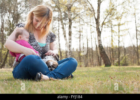 Mutter mit Baby auf dem Rasen und Welpen Stockfoto