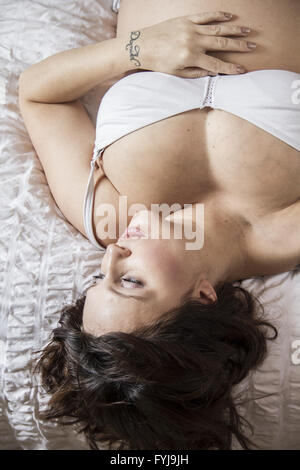 junge schwangere Frau liegend auf dem Bett, fröhliche Erwartung Stockfoto