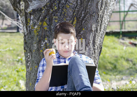 Kleiner Junge liest ein Buch im Wald mit geringer Tiefe Feld und Kopie Stockfoto