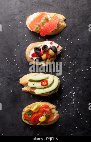 Toast-Sandwiches mit Avocado, Tomaten, Lachs und Oliven auf Stein Hintergrund. Ansicht von oben Stockfoto