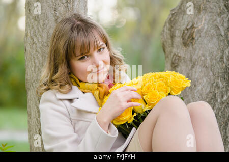 Trauriges Mädchen mit gelben Rosen, sitzt in einem Baum Stockfoto