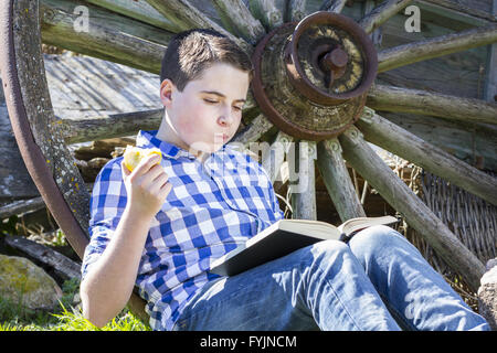 Kleiner Junge liest ein Buch im Wald einen Apfel essen Stockfoto