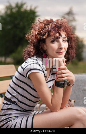 Ein schönes Mädchen sitzt auf einer Parkbank auf dem Hintergrund der grünen Natur Stockfoto