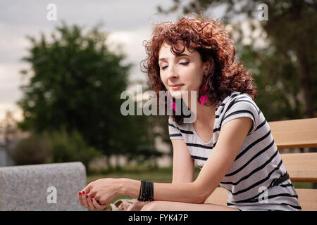 Ein schönes Mädchen sitzt auf einer Parkbank auf dem Hintergrund der grünen Natur Stockfoto