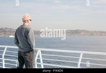 Mittleren Alter Mann gekleidet, lässig tragen Sonnenbrillen steht neben einem weißen Geländer auf einem Boot mit Blick auf das Wasser Stockfoto