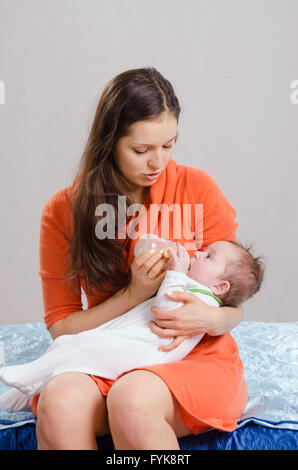 Mama-feeds von Flasche Tochter sitzt auf einem Bett Stockfoto