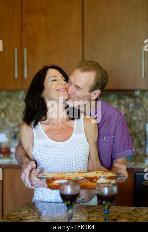 Ältere Mann und Frau umarmen und küssen in der Küche beim Abendessen vorbereiten Stockfoto