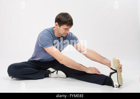 Der junge Mann dehnt Muskeln des linken Beines Stockfoto