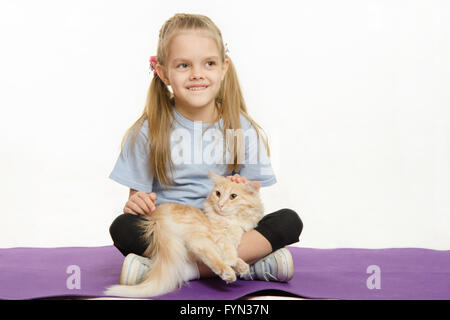 Fröhliches Mädchen sitzt auf einem Teppich mit Katze Stockfoto