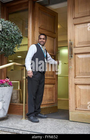 Ein Hotelpagen oder Porter Öffnen der Haustür eines Hotels für einen Gast im Vereinigten Königreich. Stockfoto