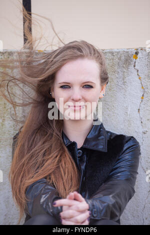 Eine Frau mit langen Wind geblasen rotes Haar draußen zu sitzen. Stockfoto