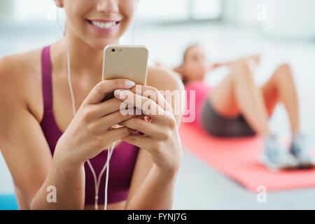 Junge lächelnde Frau im Fitnessraum entspannen und Musikhören mit einem Mobiltelefon und Kopfhörer Stockfoto