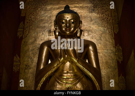 Ananda Temple Buddha Statue Bagan Myanmar // BAGAN, Myanmar — eine von vier monumentalen vergoldeten hölzernen Buddha-Statuen dominiert das Innere des Ananda Tempels, jede steht 9,5 Meter hoch auf 2,4 Meter hohen Thronen innerhalb der Kardinalnischen. Die vier Statuen stellen die Buddhas dar, die das Nirwana erreicht haben: Kakusandha, Konagamana, Kassapa und Gautama, zwei davon stammen aus dem ursprünglichen Bau des 11. Jahrhunderts und zwei wurden nach Brandschäden als Ersatz aus dem 17. Jahrhundert installiert. Diese massiven Skulpturen dienen als Brennpunkt der Hingabe im Tempel, obwohl sie lange nach dem Fundi des Tempels hinzugefügt wurden Stockfoto