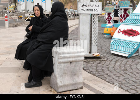 Iranische Frauen tragen schwarzen Tschador sitzen auf einer Bank am Tadschrisch-Platz in Teheran, Iran. Stockfoto